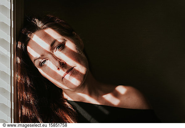 Portrait of woman beside a window with shadows across her face.