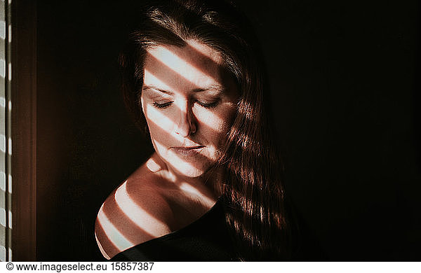 Portrait of woman beside a window with shadows across her face.
