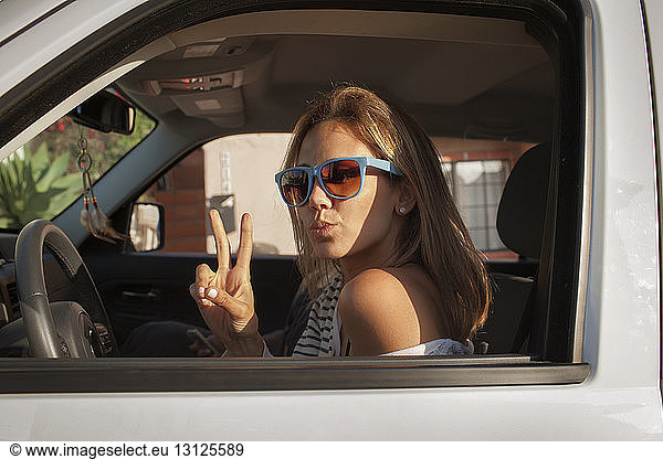 Portrait of woman gesturing peace sign while puckering lips in car