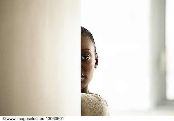 Portrait of woman hiding behind wall at home