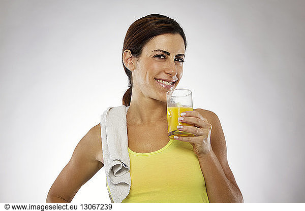 Portrait of woman holding juice glass while standing against gray background