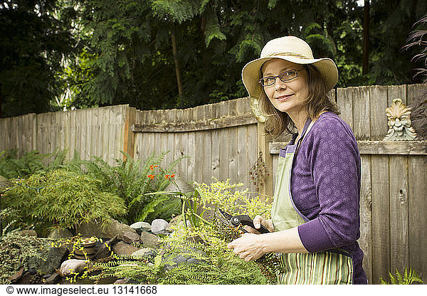 Portrait of woman holding pruning shears while standing at backyard