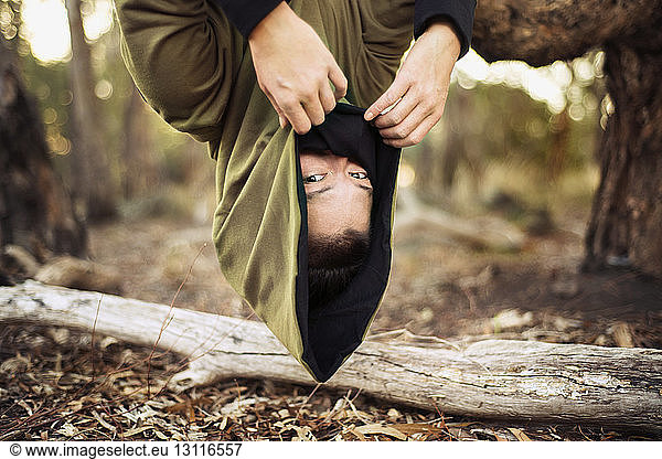 Portrait of woman in hooded jacket hanging upside down from tree