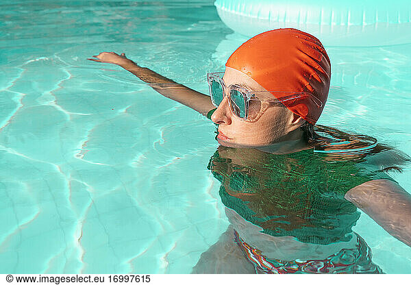 Portrait of woman in swimming pool wearing red swimming cap  green knit pullover and mirrored sunglasses