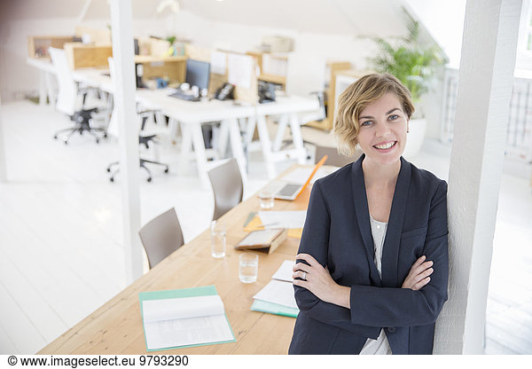 Portrait of woman leaning on column in office and smiling