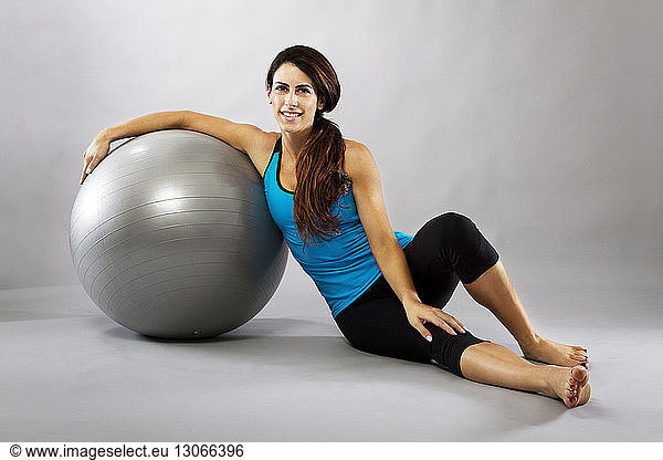 Portrait of woman leaning on fitness ball while sitting against gray background