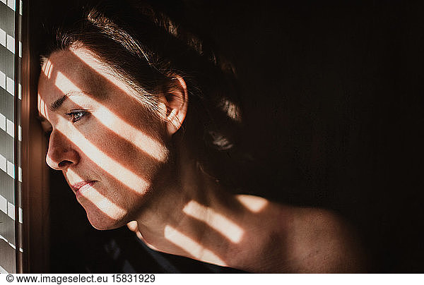 Portrait of woman looking out window with shadows across her face.
