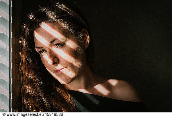 Portrait of woman looking out window with shadows across her face.