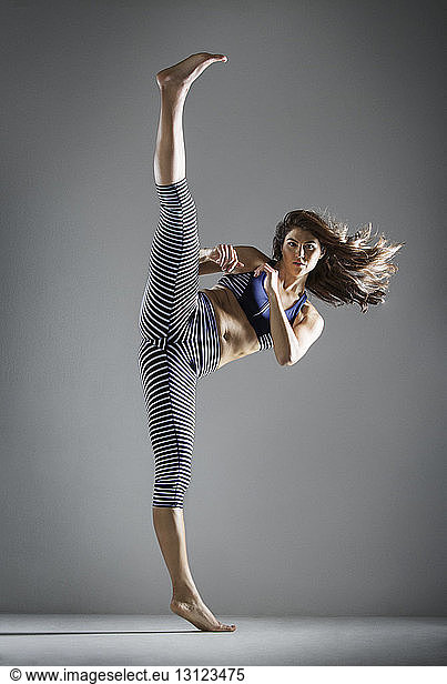 Portrait of woman practicing kick against gray background