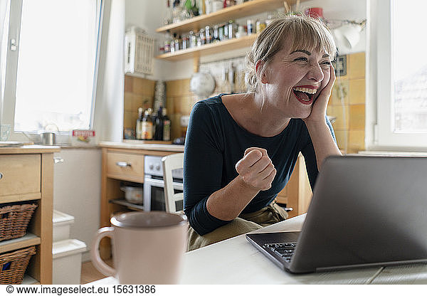 Portrait of woman sitting in the kitchen with laptop crying for joy