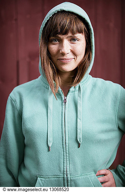 Portrait of woman wearing hood jacket standing against wall