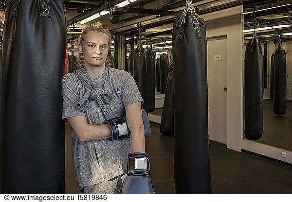 Portrait of woman with boxing gloves at sandbag in gym