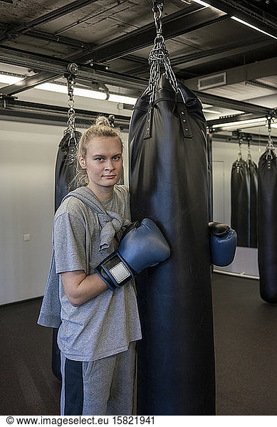 Portrait of woman with boxing gloves at sandbag in gym