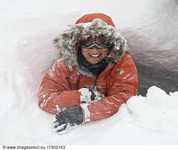 portrait of woman with faux fur hood and ski goggles in a snow hole