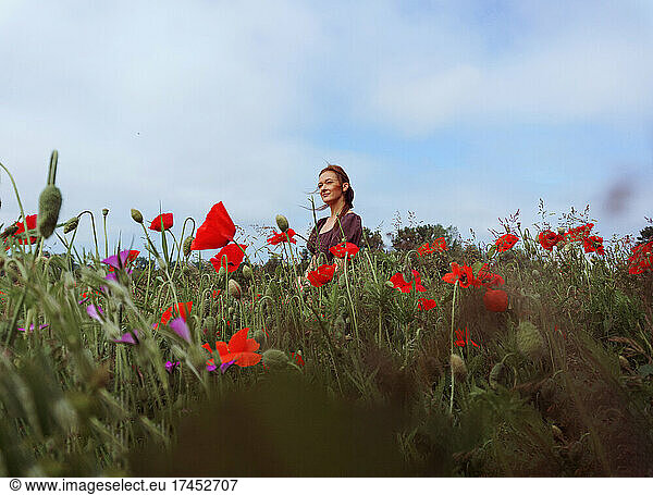 portrait of woman with hat standing among green grass and red flowers