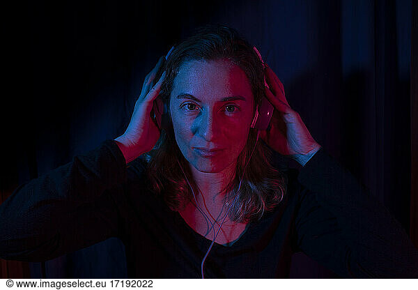 Portrait of woman with headphones set with red and blue neon lights.
