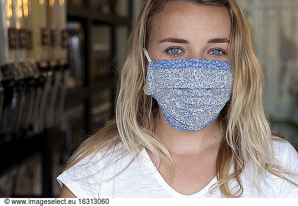 Portrait of young blond woman wearing face mask  standing in waste free wholefood store.