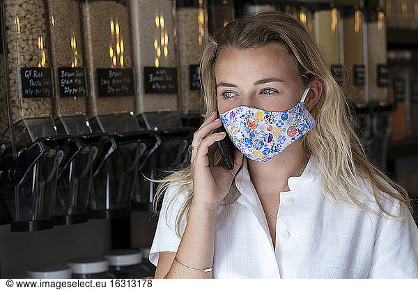 Portrait of young blond woman wearing face mask  standing in waste free wholefood store.