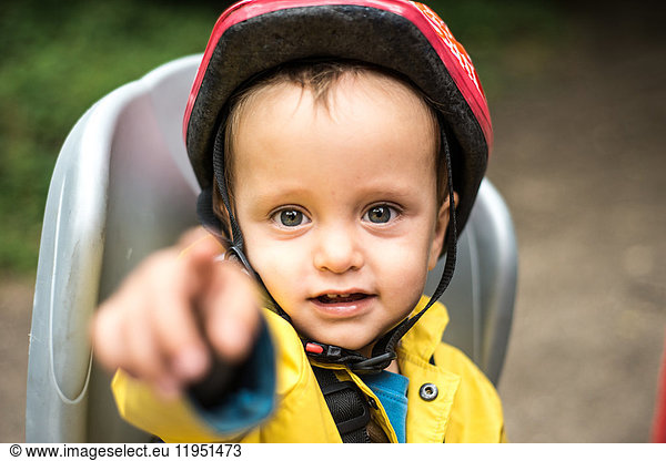 Portrait of young boy sitting in child's seat of adult bicycle pointing