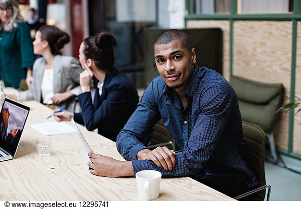 Portrait of young businessman sitting with female colleagues at table in office meeting