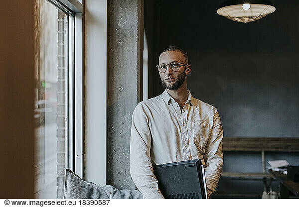 Portrait of young businessman with laptop standing in startup company