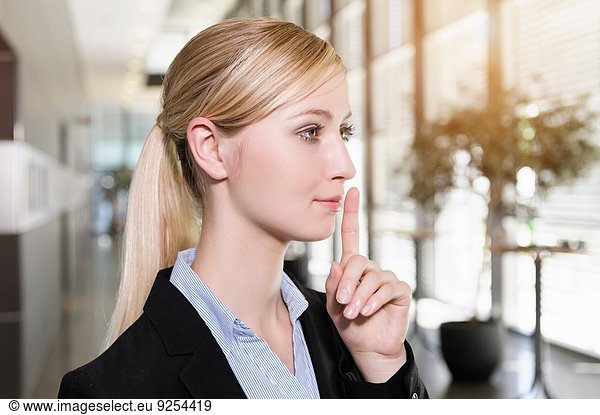 Portrait of young businesswoman holding finger up to lips