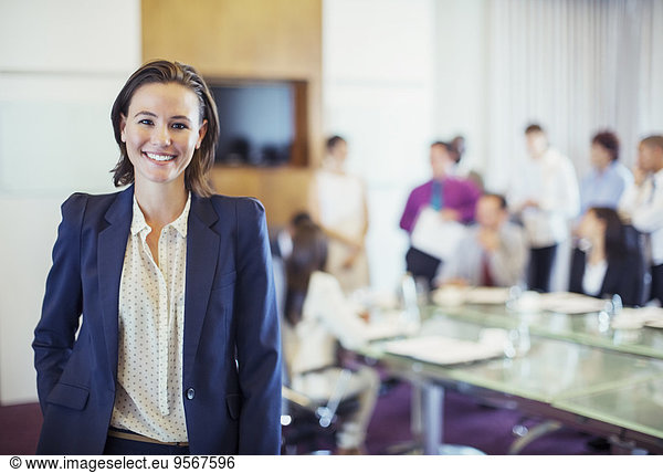 Portrait of young businesswoman smiling in conference room  people in background