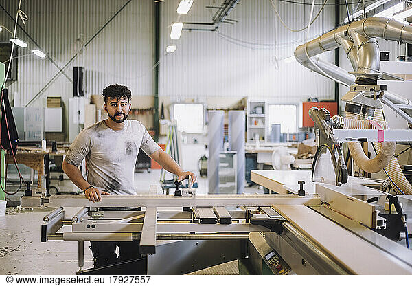 Portrait of young carpenter standing by machinery in workshop