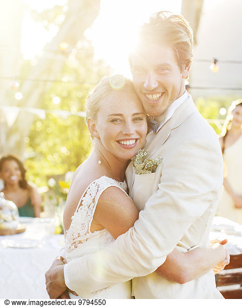 Portrait of young couple embracing in garden during wedding reception