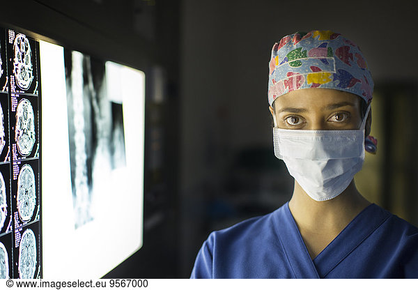 Portrait of young female doctor standing near screen with MRI image