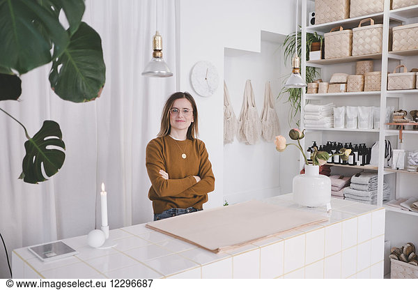 Portrait of young female entrepreneur standing arms crossed at desk in studio