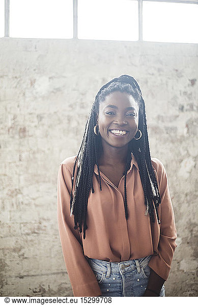 Portrait of young female IT expert smiling while standing against wall in office