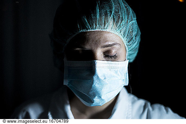 Portrait of young female surgeon  wearing mask and a surgical mask  in front of black background