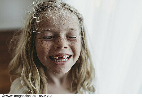Portrait of young freckled smiling girl missing tooth with eyes closed