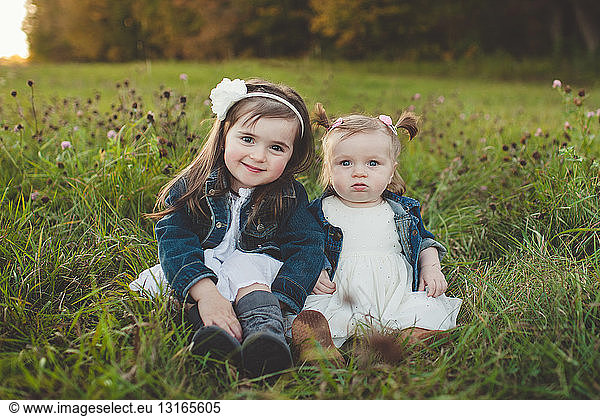 Portrait of young girl and baby sister in field