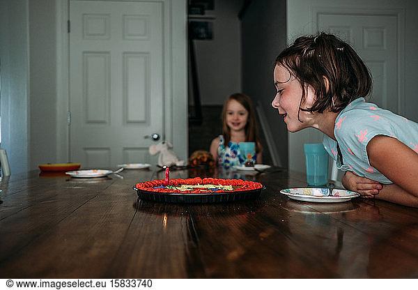portrait of young girl blowing out birthday candle at a table