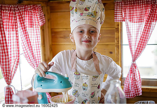 Portrait of young girl dressed in chef's outfit in wendy house pretending to cook in kitchen