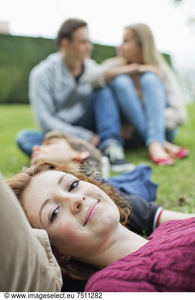 Portrait of young girl with head on boy's stomach and couple sitting in background at park