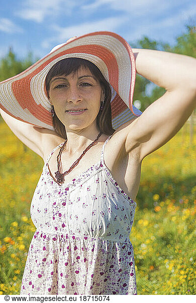 Portrait of young lovely woman wearing straw hat in the flower meadow while looking camera smiling