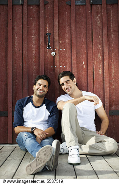Portrait of young male friends sitting in front of wooden wall