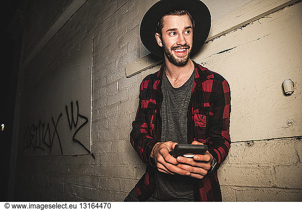 Portrait of young male hipster leaning against wall at night