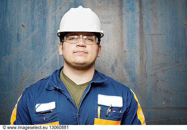 Portrait of young male worker standing against metal wall at recycling plant