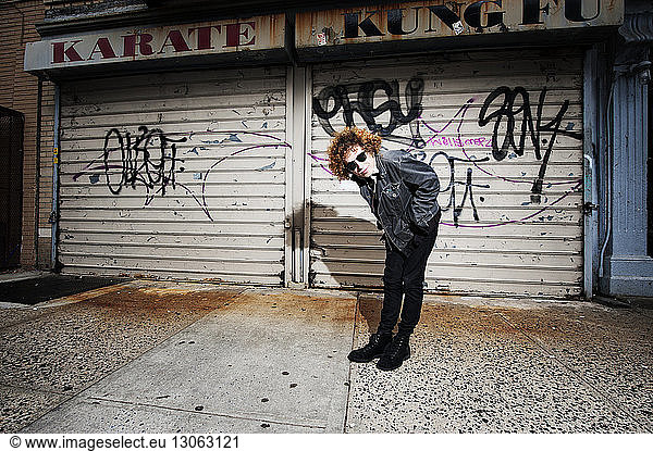Portrait of young man bending on footpath against graffiti shutters