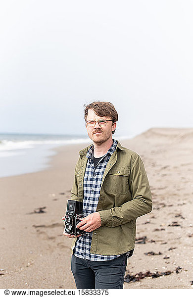 Portrait of young man holding film camera on beach