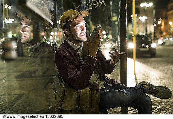 Portrait of young man on the phone sitting at bus stop by night  Lisbon  Portugal