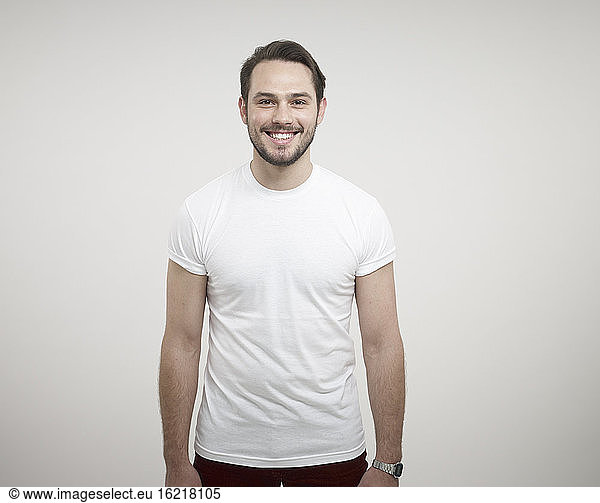 Portrait of young man standing against white background  smiling