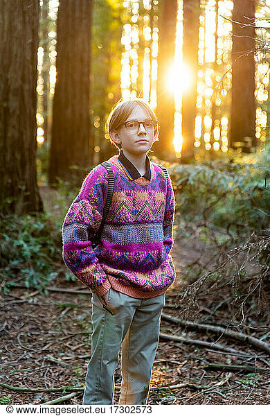 Portrait of young person standing in forest with sun setting