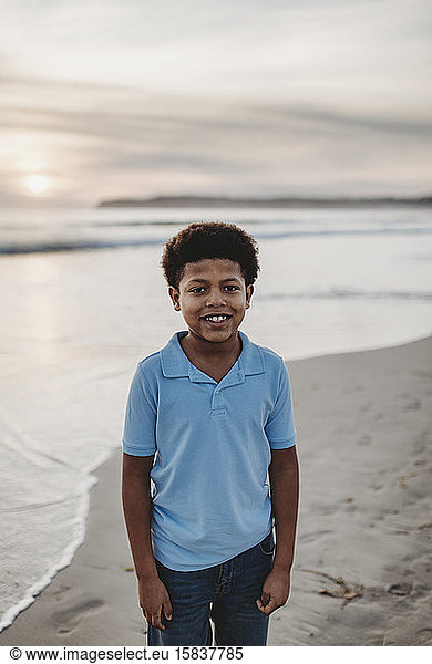 Portrait of young school-aged boy smiling at beach during sunset