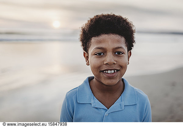Portrait of young school-aged boy smiling at beach during sunset