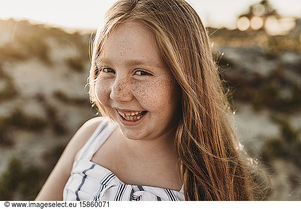 Portrait of young smiling redhead girl with freckles at beach sunset